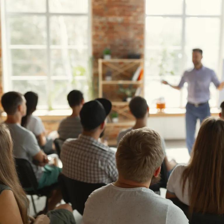 Male speaker giving presentation in hall at university workshop. Audience or conference hall. Rear view of unrecognized participants in audience. Scientific conference event, training. Education concept.