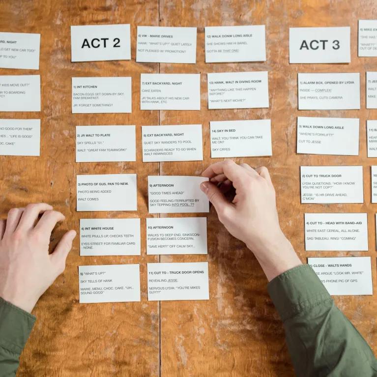 Hands arranging screenplay cards on a wooden table, depicting script development.