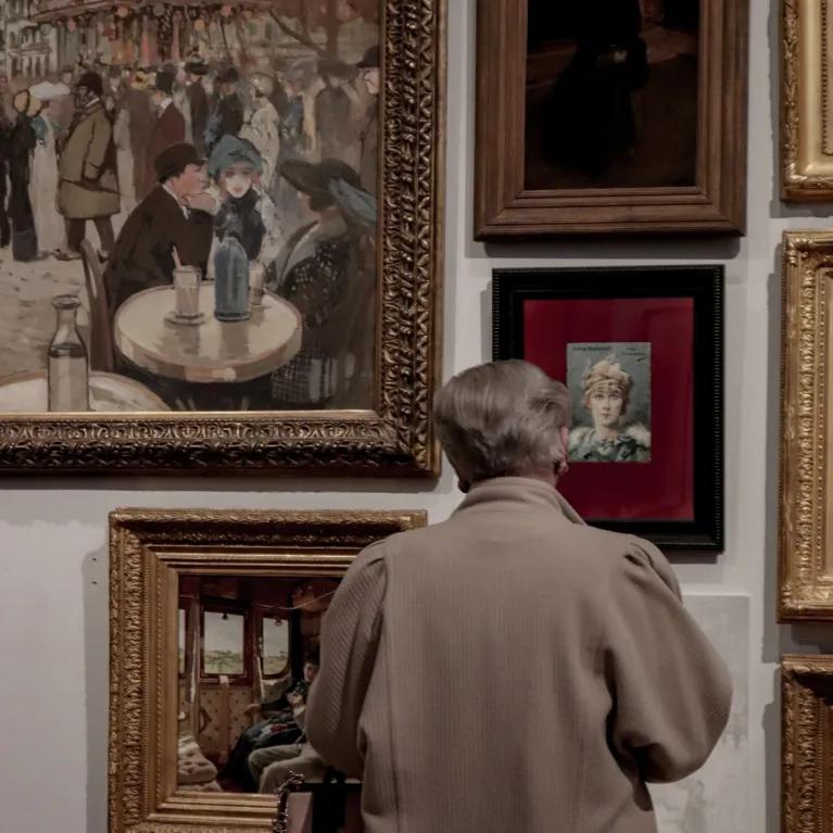 A man standing, looking at some paintings on a wall