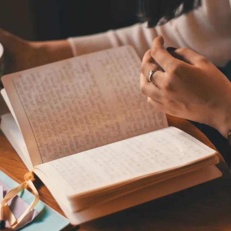 Photo of a person reading a book and holding a cup of tea