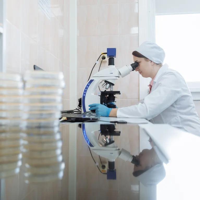 Female scientist using a microscope in a laboratory environment, focusing on research.