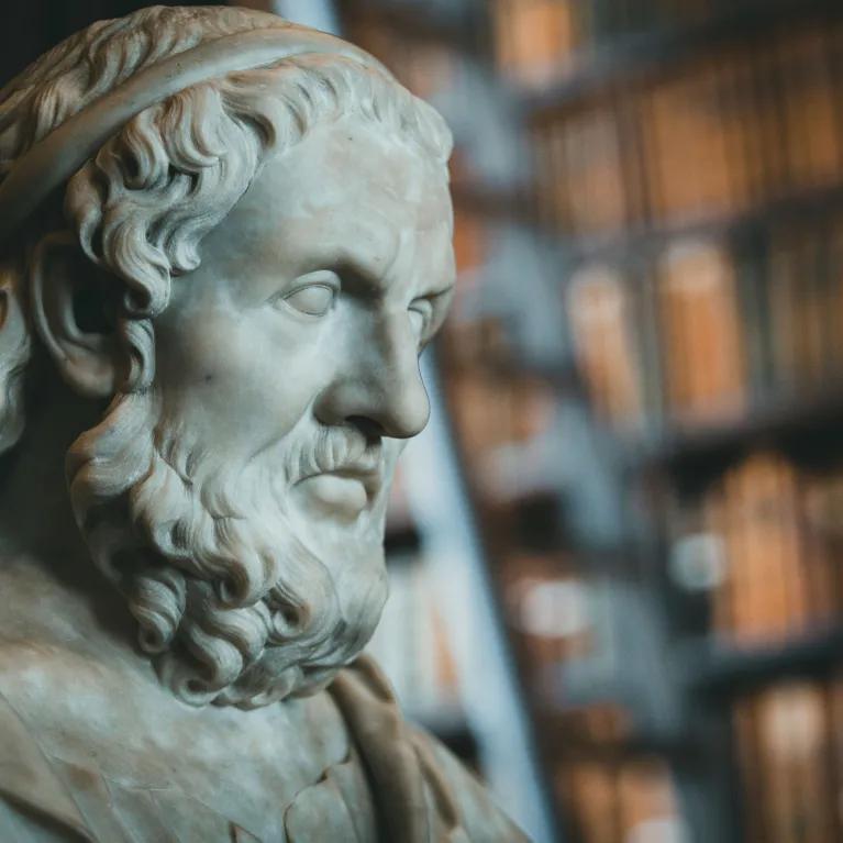 Close-up of a classical marble statue with blurred bookcases in the background