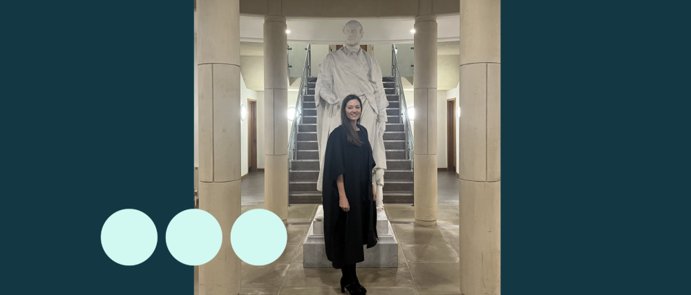 Woman in graduation gown stood in front of a statue 