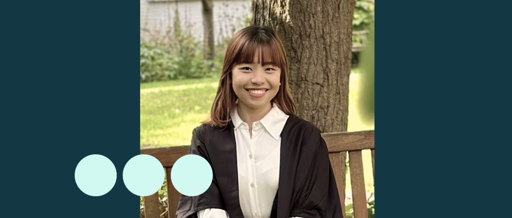 Asian woman sat on bench in graduation gown